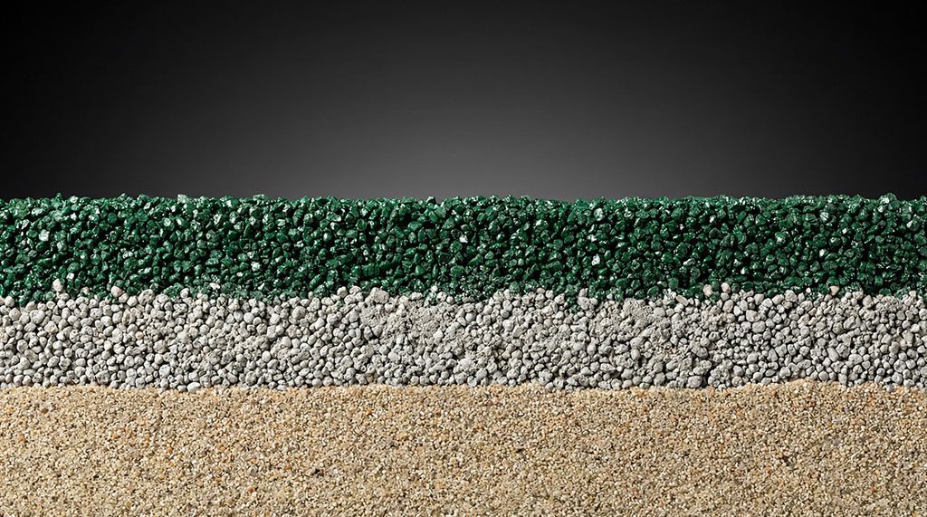 Close-up cross-section of artificial turf infill showing coated sand settled at the base of the pile